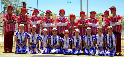 The WA Done dance team in traditional red and blue Karen dress, lined up in two rows outdoors.