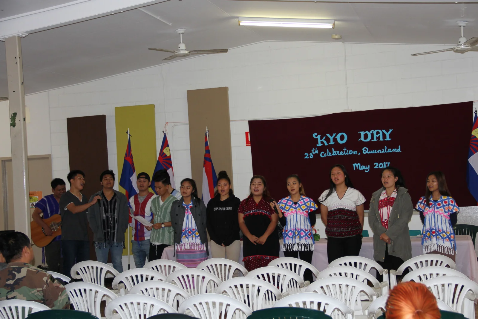 Young people singing on stage in front of a banner reading "KYO Day, 28th celebration, Queensland, May 2017".