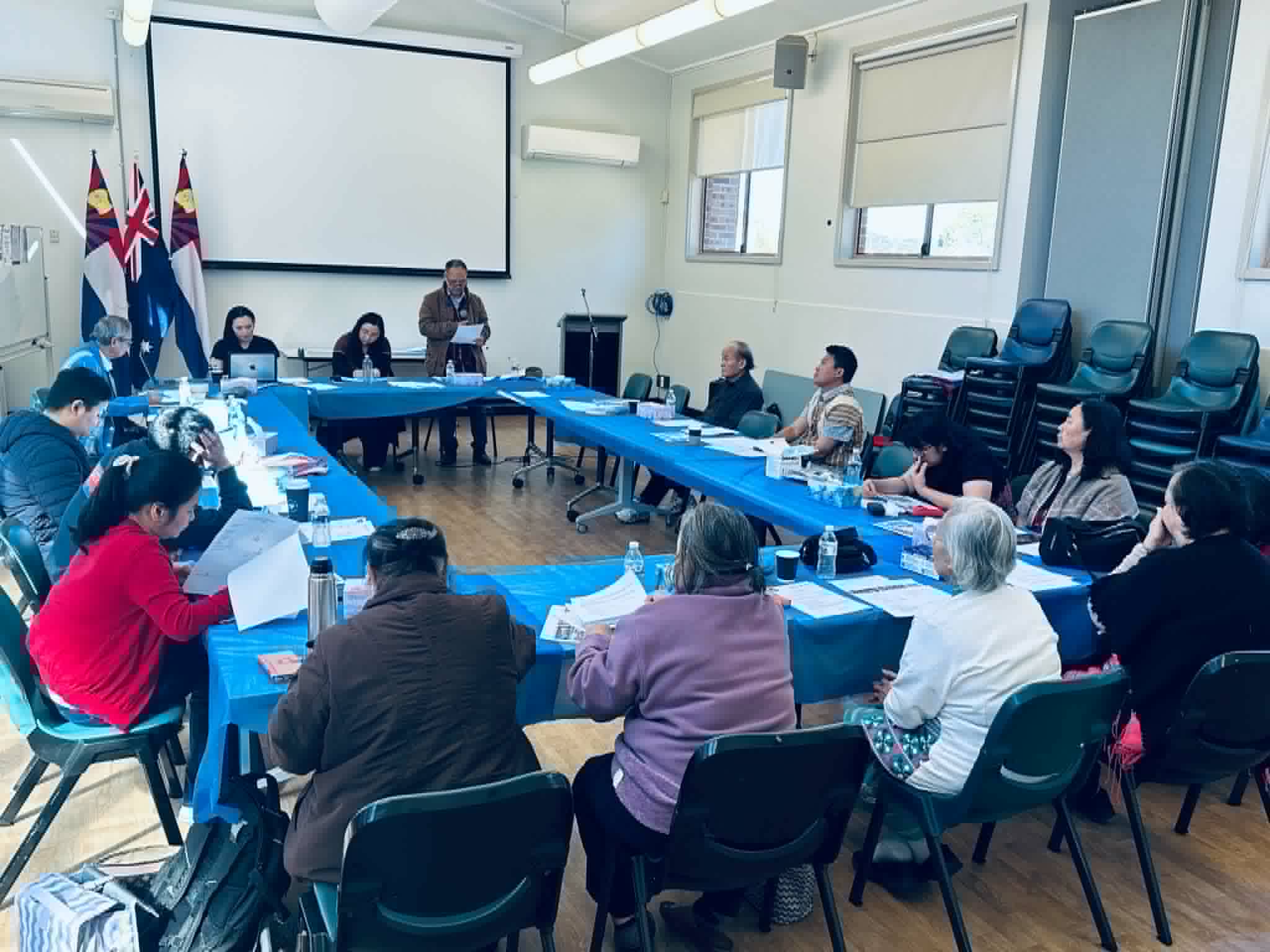 Members seated around tables set in a U shape at the NSW branch's annual general meeting, with the Australian and Karen flags.